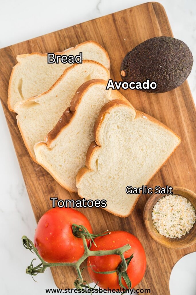 Avocado tomato sandwich ingredients laid out on a wood cutting board. The tomatoes and avocado have not been cut yet.