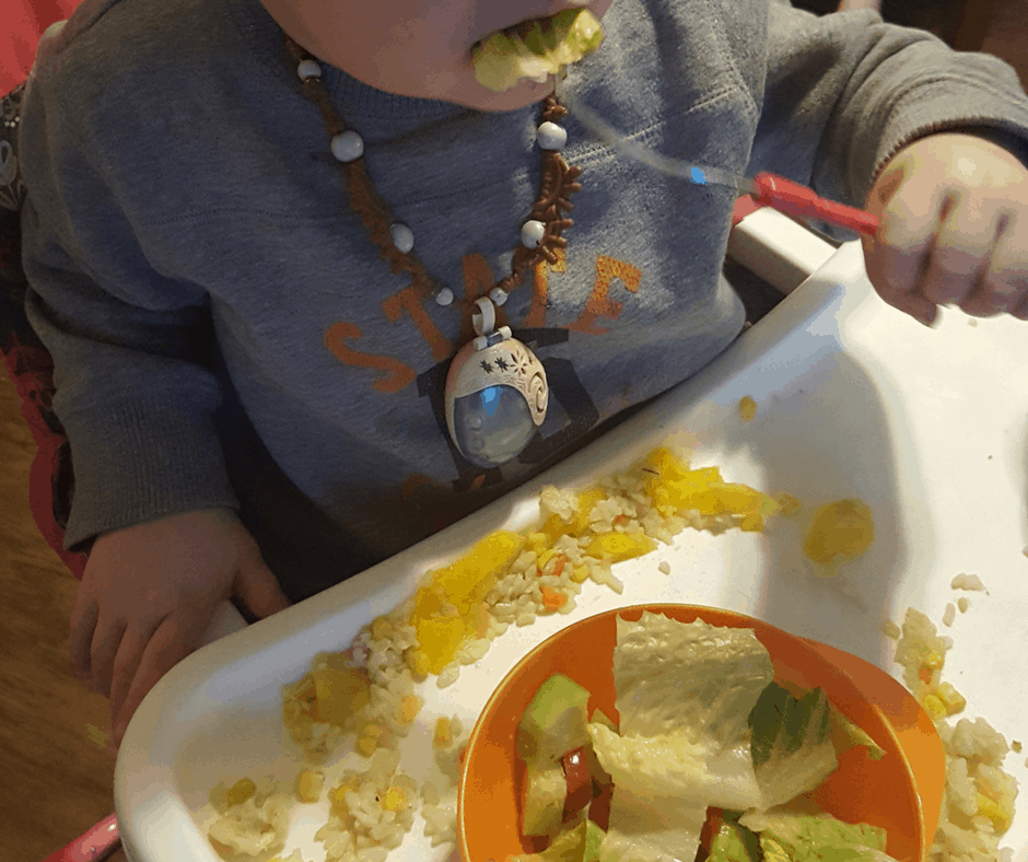 get toddlers to eat veggies, toddler eating veggies, a salad, in highchair, wearing moana necklace