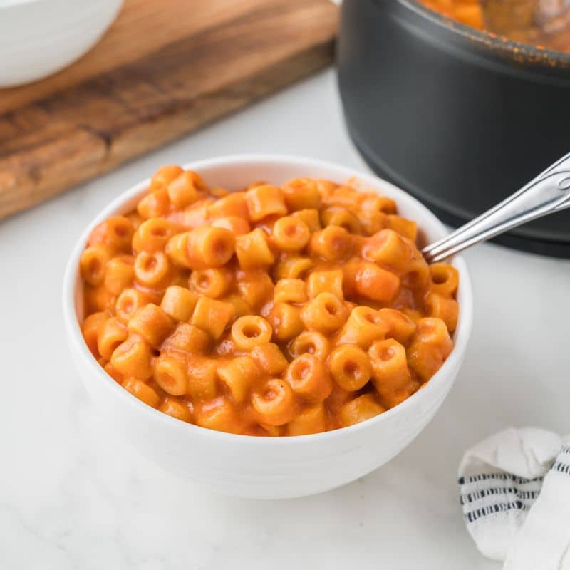 Vegan Spaghettios in a white bowl next to a medium sized dark gray saucepan that was used to make it from scratch.
