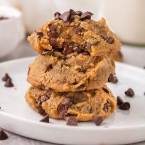 Chocolate Chip Chickpea Cookies stacked on a white plate with a bite out of the top one, with melty chocolate.