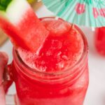 Watermelon slushie in a glass with watermelon slice and blue cocktail umbrella.