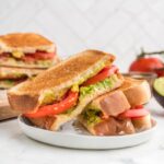Avocado sandwich on a white plate, cut in half and overlapping each other.