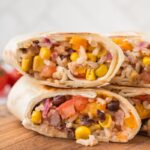 Black Bean and brown rice vegan burritos sliced in half sitting on top of each other on a cutting board.