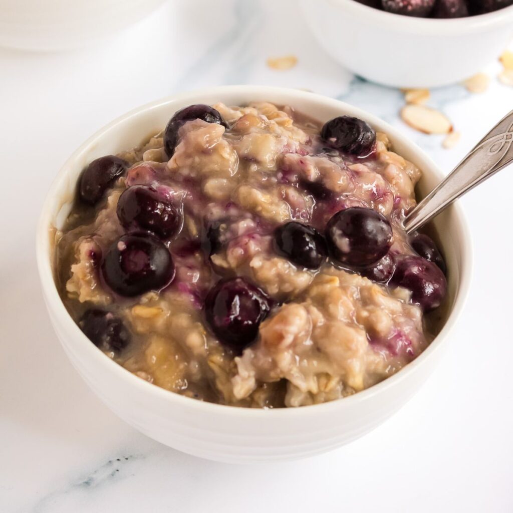 Healthy blueberry oatmeal in a white bowl with extra blueberries on top.