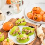 Apple monsters, clementine pumpkins, and banana ghosts, all arranged together on a cutting board for a kids Halloween party.