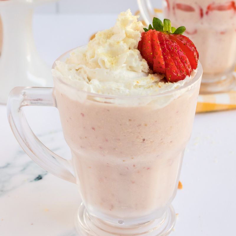 Vegan Strawberry Cheesecake Milkshake in a clear glass with strawberries topping it.