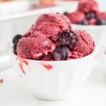 Berry Ice Cream scooped into a white dish with extra frozen berries.