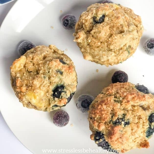 Blueberry muffins with oats, alphabet snacks that start with b, these 3 blueberry muffins are shown from an overhead angle, have blueberries surrounding them and are on a white plate.