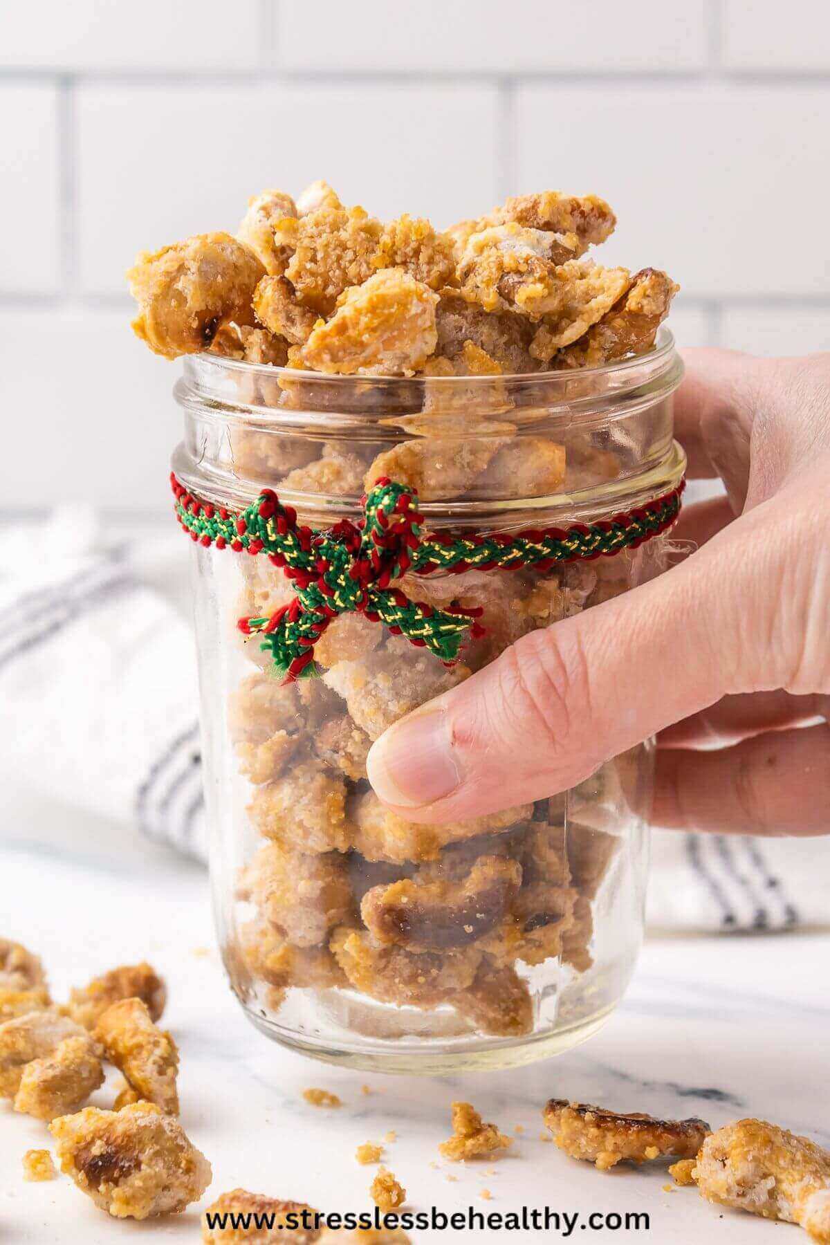 Hand holding candied cashews in holiday decorated small mason jar as a homemade gift.