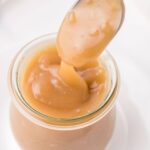 Vegan caramel sauce drizzling from a spoon into a small glass jar.
