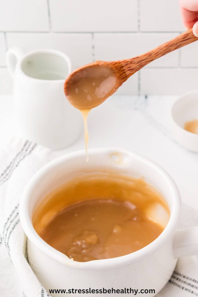 Vegan caramel sauce being drizzled off a wood spoon into a small white sauce pan.