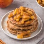 Vegan Apple Pancakes on a plate with soft apples and maple syrup on top.