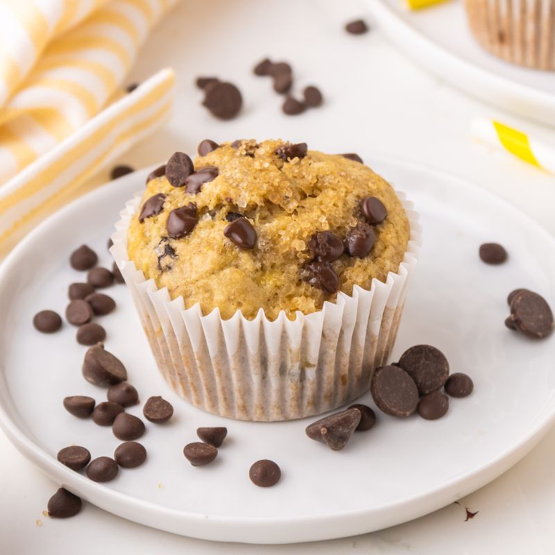 1 banana chocolate chip muffin on a white plate surrounded by more chocolate chips.