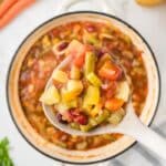 Vegan Minestrone Soup in a white dutch oven with some lifted up on a ladle.