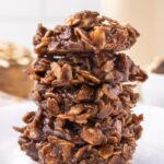 Vegan no bake chocolate oatmeal cookies stacked on top of each other with more cookies and milk behind the stacked cookies.