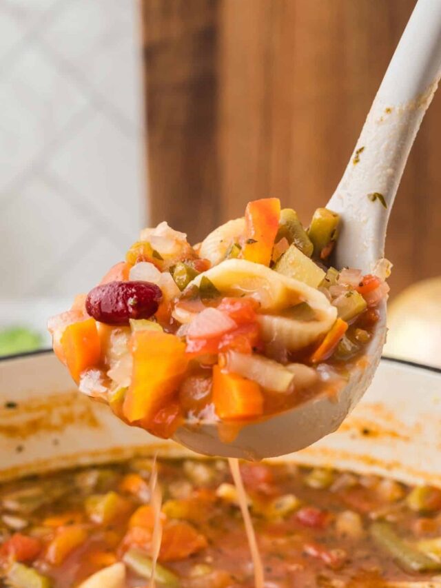 Close up of a ladle above a white dutch oven with Vegan Minestrone Soup in it and in the ladle.