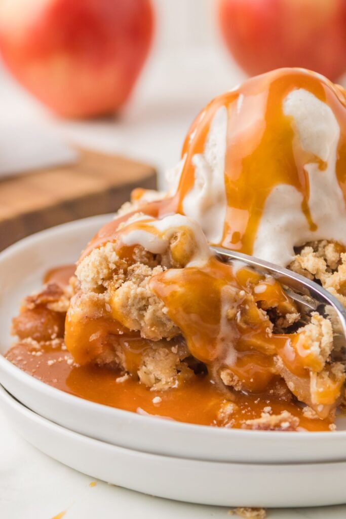 Vegan Apple Pie Bar with melting vegan vanilla ice cream and homemade caramel sauce on top, on a white plate with a piece being cut with a fork.