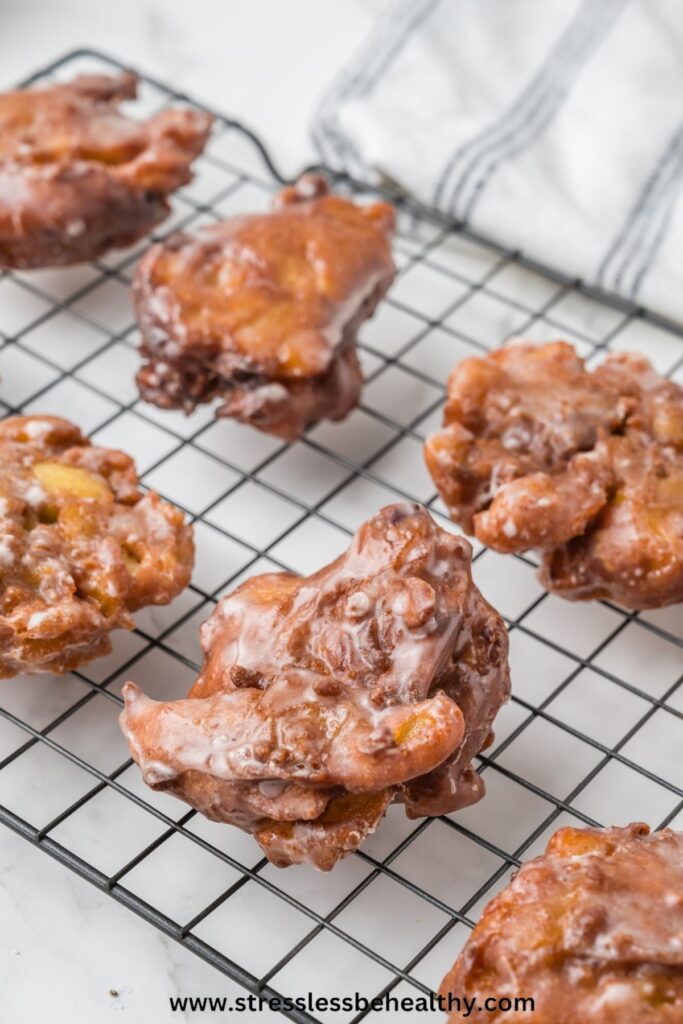 Vegan apple fritters cooling on a cooling rack after having been dipped in icing.