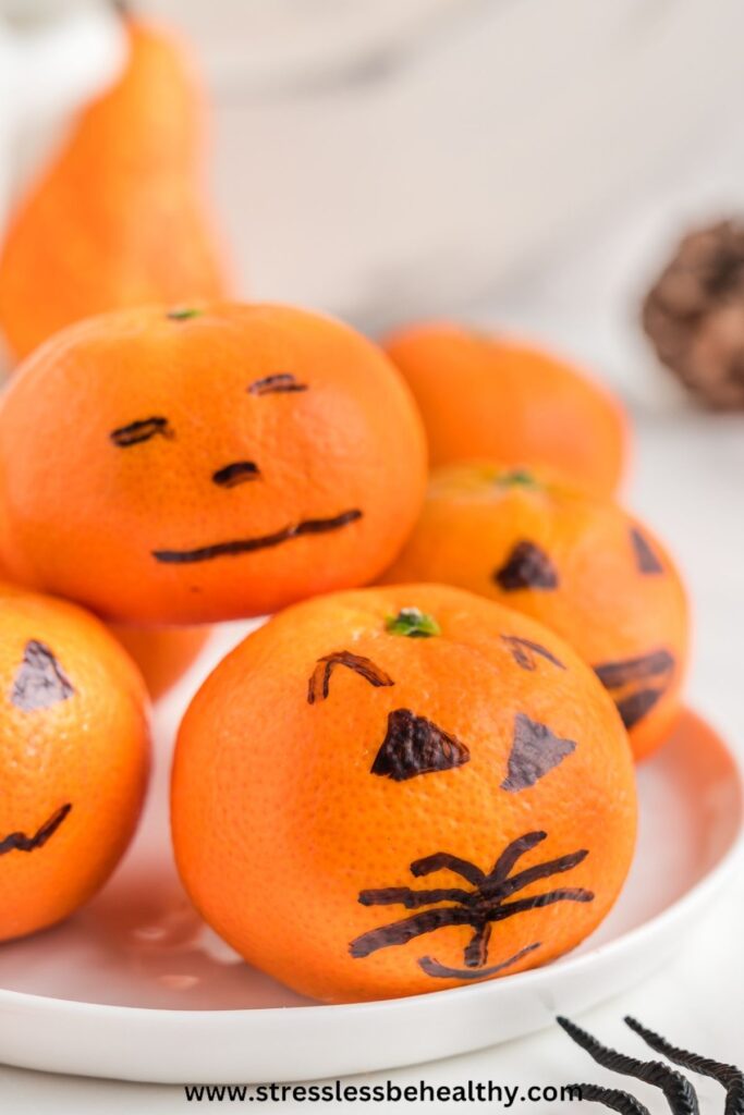 Clementine pumpkins with cute jack-o-lantern drawn on faces pile on top of each other on a plate.