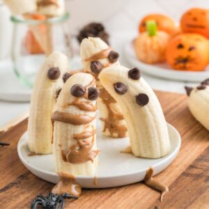 Halloween banana ghosts and banana mummies on a white plate on a cutting board.