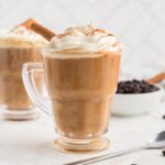 Vegan pumpkin spice latte with non-dairy whip, a sprinkle of pumpkin pie spice, and a cinnamon stick in a mug.