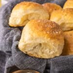Vegan dinner rolls in a bread basket with a blue-gray linen underneath.