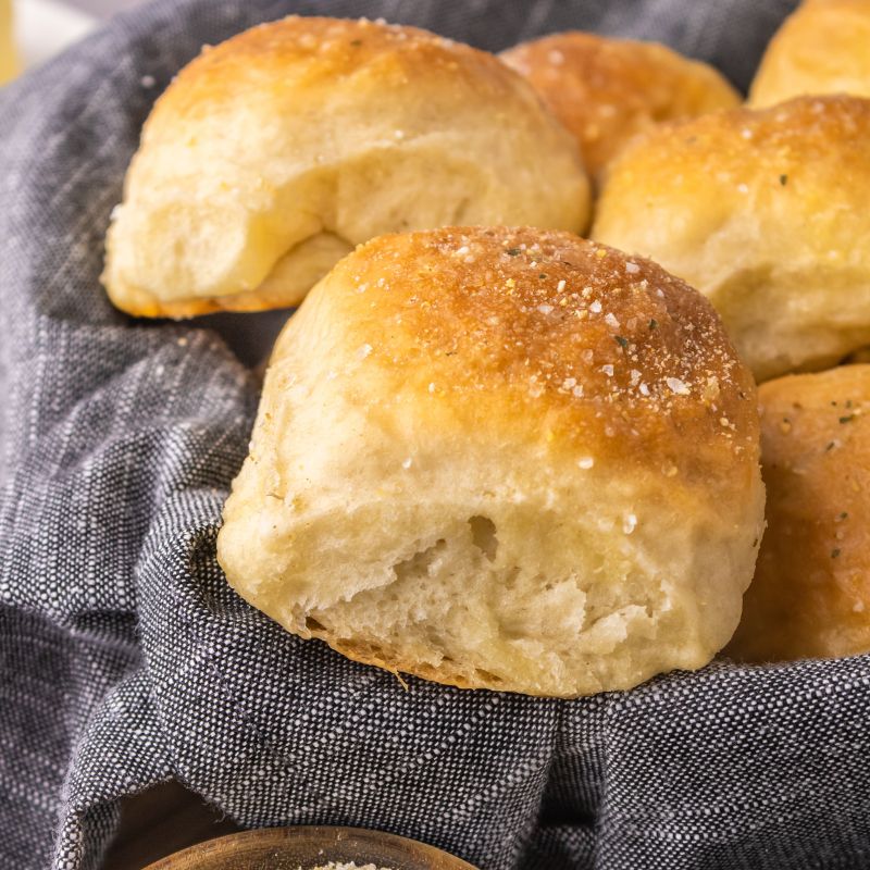 Vegan dinner rolls in a bread basket with a blue-gray linen underneath.