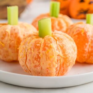 4 clementine pumpkins with celery stick stems on a white plate.