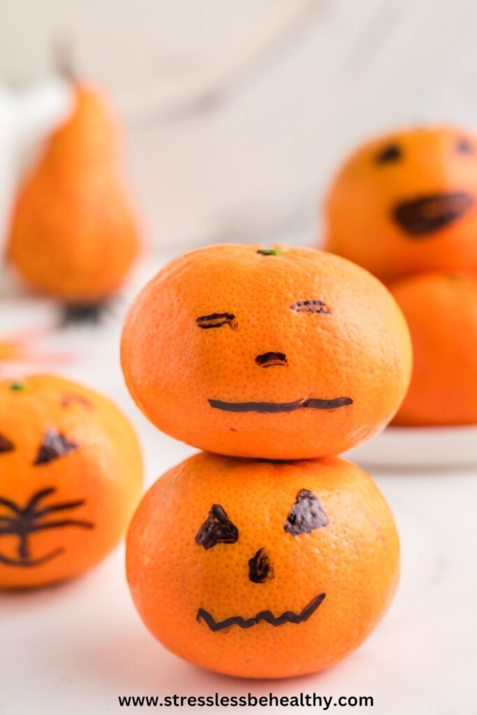 2 cute Halloween Pumpkin jack-o-lanterns sitting on top of each other, with more in the background.