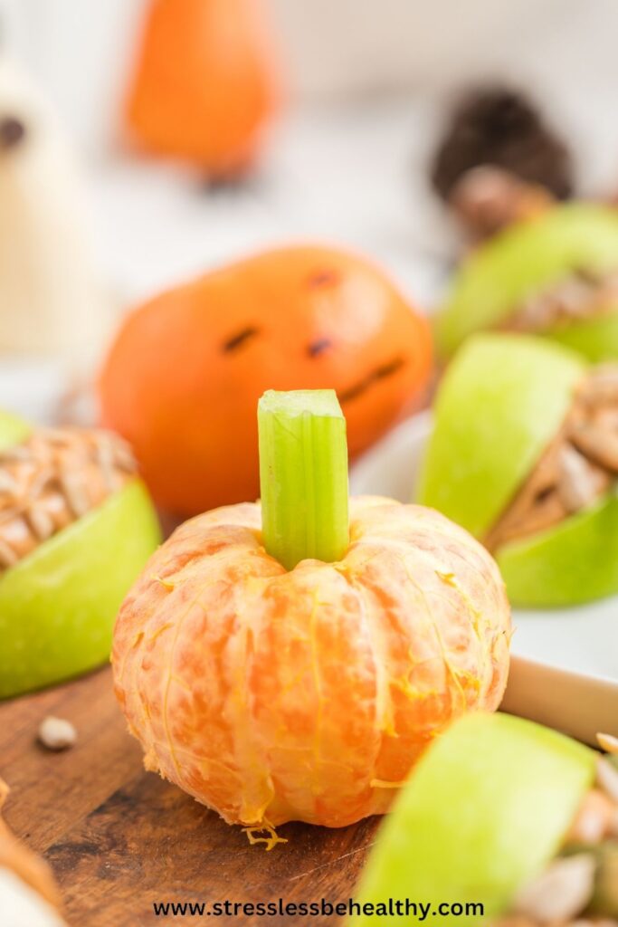 Clementine pumpkin, peeled with a celery 'stem' sitting on a wood cutting board with other healthy halloween treats.