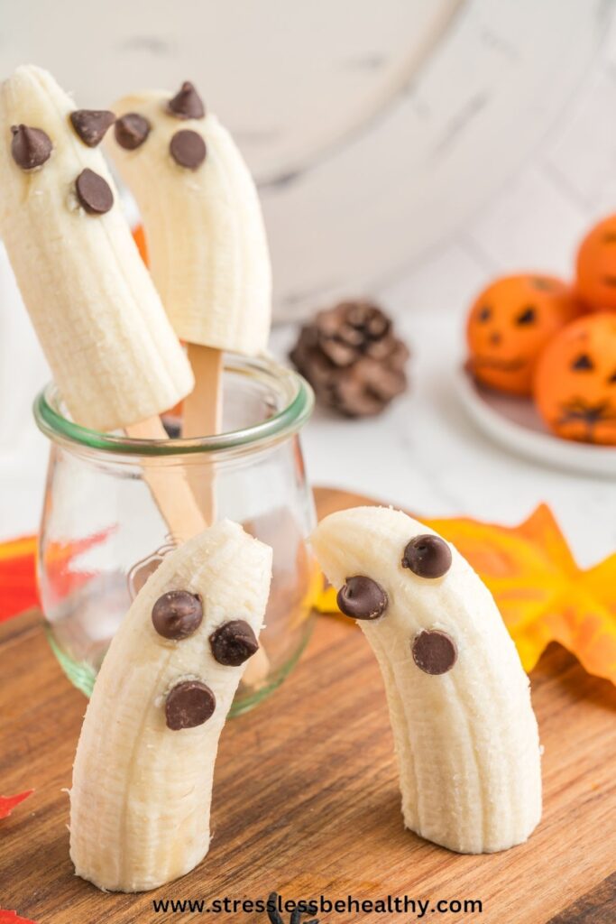 2 banana ghost popsicles in a jar with two banana ghosts not on a stick sitting on a cutting board.