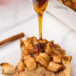 Apple french toast casserole slice with maple syrup pouring down on it.