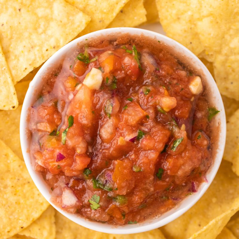 Homemade salsa in a white bowl in the middle of a bunch of tortilla chips.