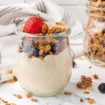 Vanilla almond granola on top of non-dairy yogurt in a weck jar, with strawberries an blueberries on top, as well.