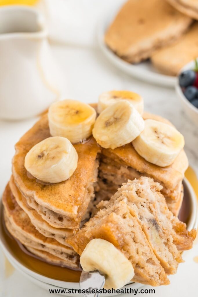 Banana pancakes with a slice cut out and on a fork laying next to the rest of the stacked vegan pancakes