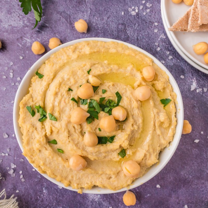Homemade hummus in a white bowl with parsley, olive oil, and whole chickpeas added to the top.