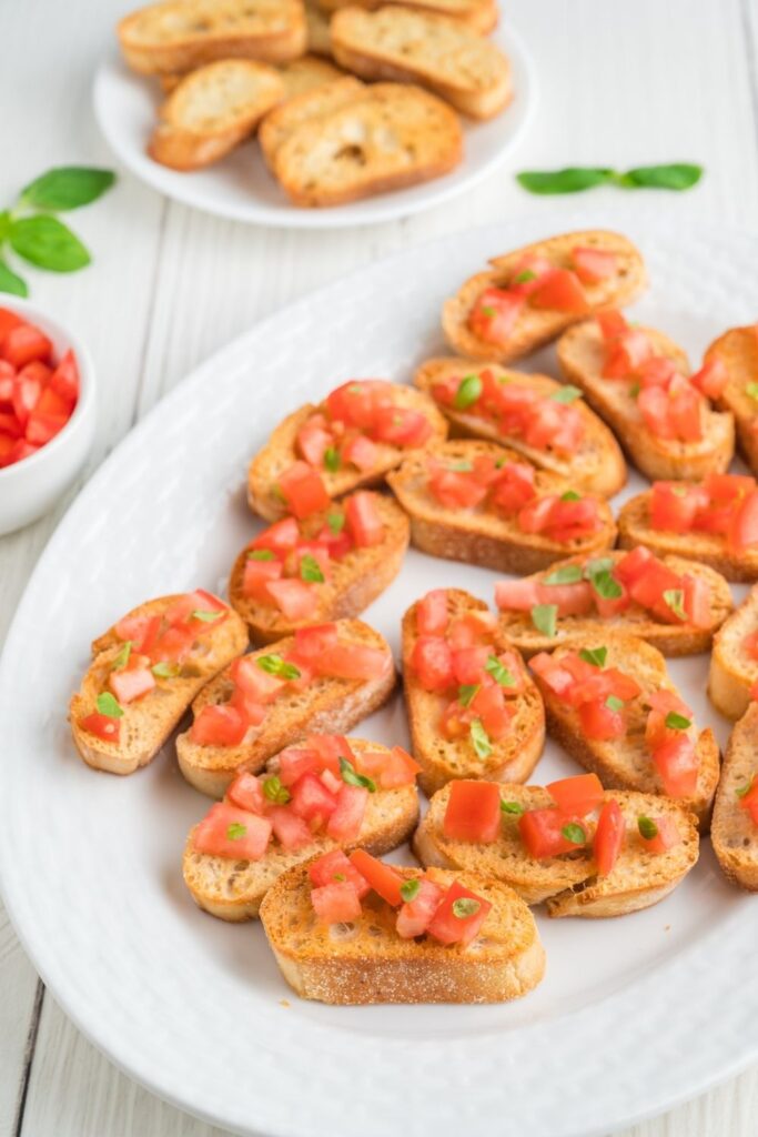 Vegan crostini with tomato and basil on top on white oval serving dish.