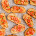Vegan crostini with tomato and basil on top on parchment paper.