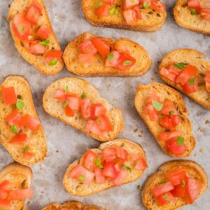Vegan crostini with tomato and basil on top on parchment paper.