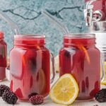2 cups of blackberry lemonade with handles, with blackberries and a lemon slice leaning against the glasses.