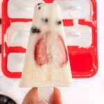 Coconut fruit popsicle being held with popsicle mold in the background.