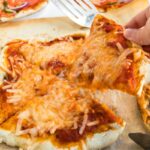 Taking a slice of vegan cheese pizza from a whole vegan pizza.