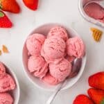 Vegan Strawberry Ice Cream in a white bowl with more strawberries around the bowl.