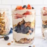 Vegan parfait with layers including granola, almond milk yogurt, blueberries, and strawberries, in a small mason jar.