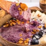 Close up of a blueberry smoothie bowl with some on a coconut spoon and the rest in a coconut bowl.