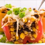 Quinoa stuffed peppers on a white plate, pepper is cut in half to see the insides.
