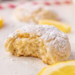Vegan Lemon cookie with a bite taken out of it surrounded by lemon slices and powdered sugar.