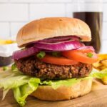 Black bean burger with veggies on a wood cutting board with fries behind it.