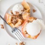 Baked apples on a white plate with non-dairy vanilla ice cream topping them.