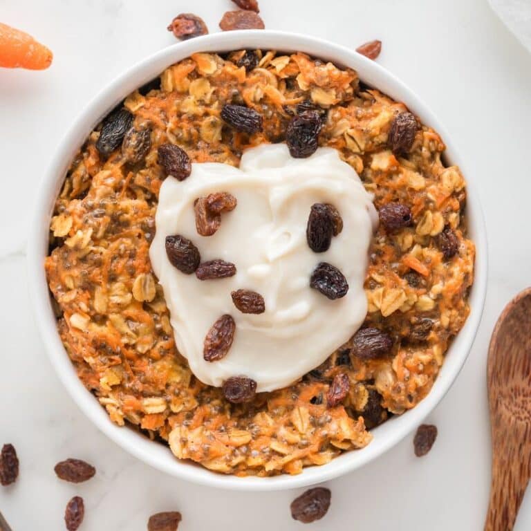 Carrot cake oatmeal with cream cheese topping and raisins in white bowl.